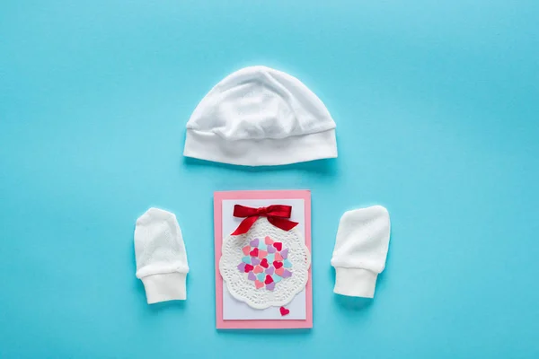 Top view of greeting card and baby hat and mittens on blue background, concept of mothers day — Stock Photo