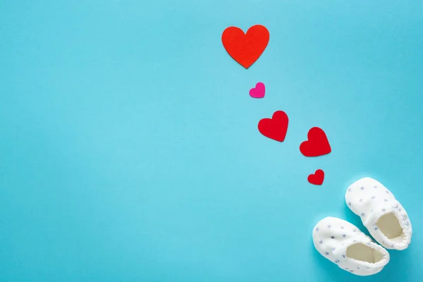 Vista superior de botines de bebé con corazones de papel sobre fondo azul, concepto de día de las madres - foto de stock