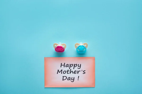 Top view of greeting card with happy mothers day lettering and pacifiers on blue background — Stock Photo