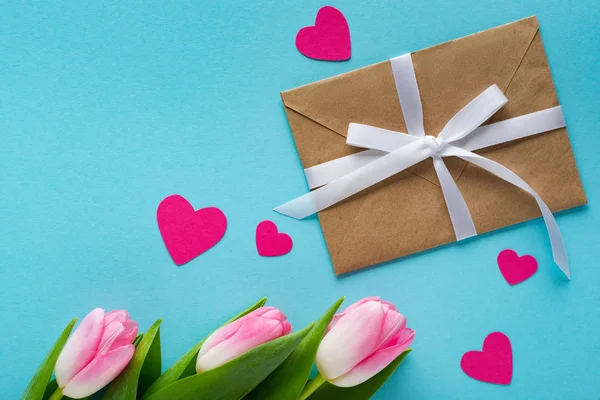 Верхний вид конверта, бумажных сердец и тюльпанов на голубом фоне — стоковое фото