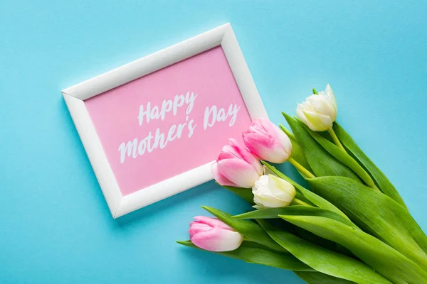 Vista superior de los tulipanes en el marco con letras felices del día de las madres sobre fondo azul - foto de stock