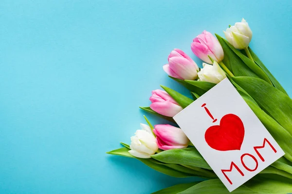 Vista superior de la tarjeta de felicitación con i love mamá letras en ramo de tulipanes sobre fondo azul - foto de stock