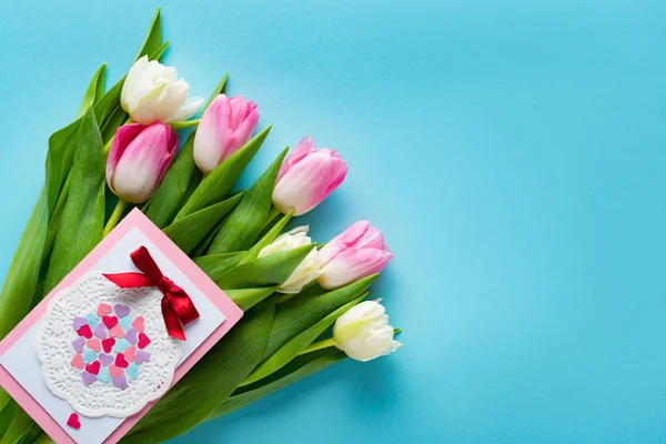 Top view of greeting card on tulips on blue surface — Stock Photo