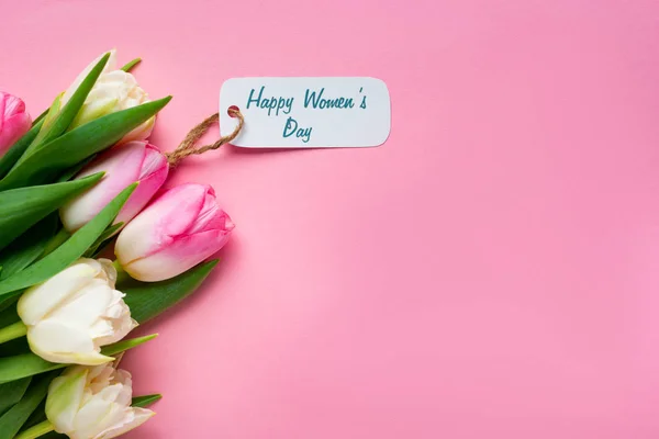 Vue du dessus du bouquet de tulipes avec joyeux lettrage de jour pour femmes sur étiquette en papier sur surface rose — Photo de stock