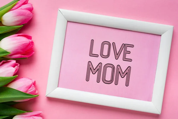 Vista superior de amor mamá letras en el marco cerca de tulipanes sobre fondo rosa - foto de stock