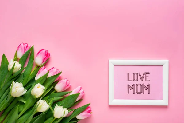 Vista dall'alto di tulipani e cornice con amore mamma lettering su superficie rosa — Foto stock