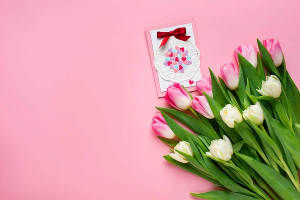 Vista superior de la tarjeta de felicitación cerca del ramo de tulipanes sobre fondo rosa - foto de stock