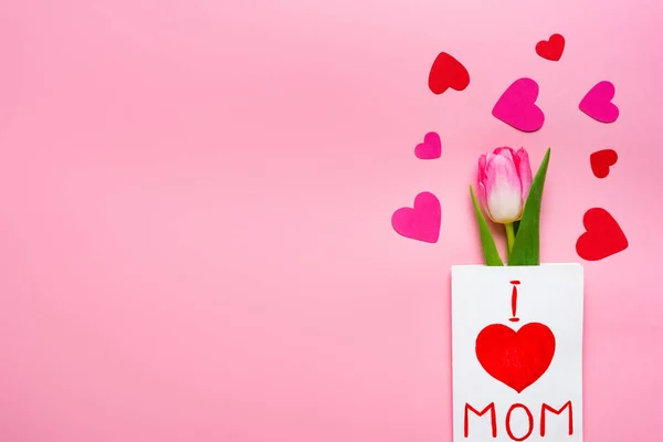 Top view of greeting card with i love mom lettering, tulip and paper hearts on pink background — Stock Photo