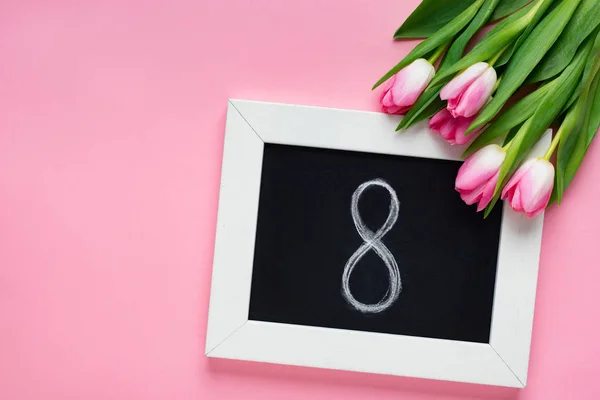 Top view of chalkboard with 8 number near tulips on pink background — Stock Photo