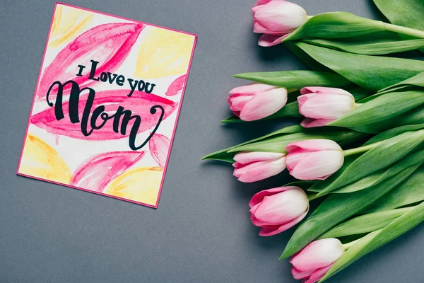 Vista superior del ramo de tulipanes y tarjeta de felicitación con te amo mamá letras sobre fondo gris - foto de stock