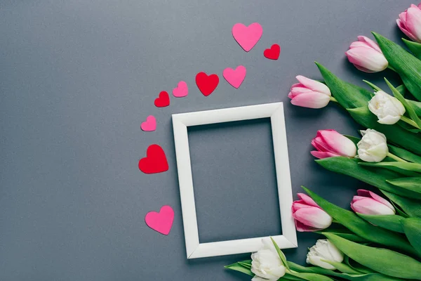 Top view of white frame with paper hearts and tulips on grey surface — Stock Photo