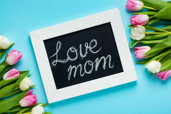 Vue du dessus du tableau avec l'amour maman lettrage et tulipes sur la surface bleue — Photo de stock