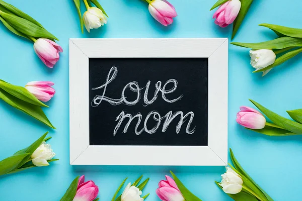 Top view of tulips around chalkboard with love mom lettering on blue background — Stock Photo