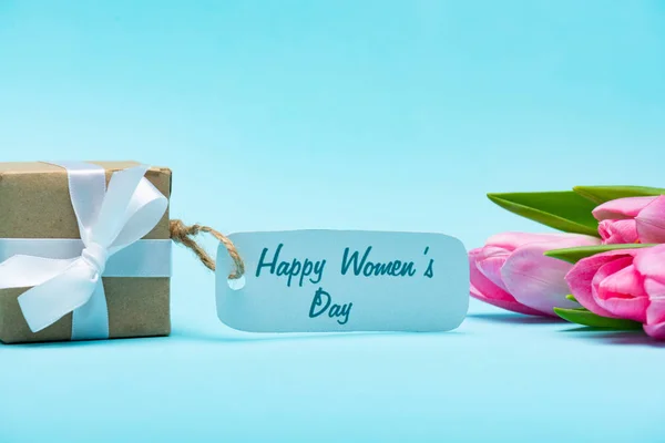 Gift box with happy womens day lettering on paper label and tulips on blue background — Stock Photo