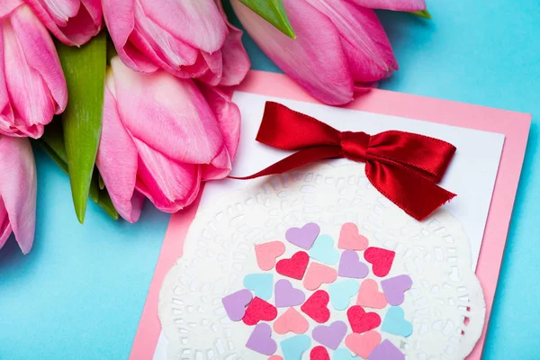 Vista da vicino del biglietto di auguri con fiocco e tulipani su sfondo blu — Foto stock