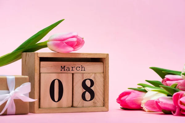 Wooden calendar with 8 march date near gift box and tulips on pink background — Stock Photo