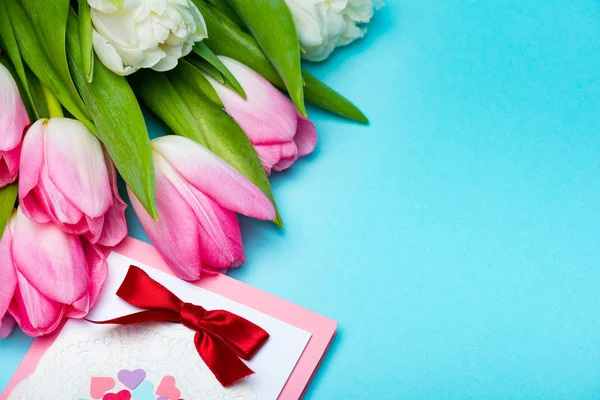 Vista da vicino di mazzo di tulipani vicino a biglietto di auguri su superficie azzurra — Foto stock