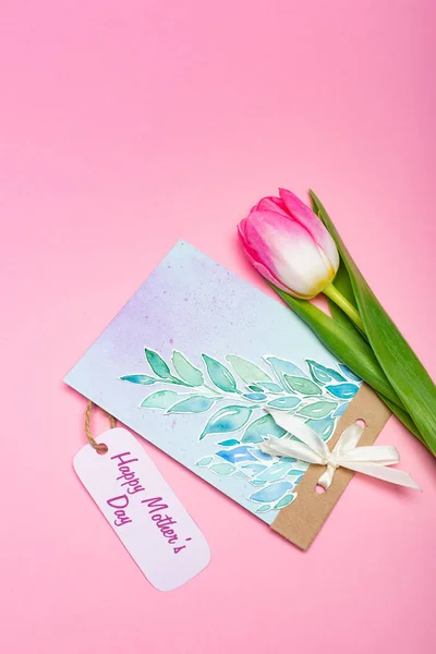 Vista dall'alto di disegno biglietto di auguri con felice giorno delle madri lettering su etichetta di carta e tulipano su sfondo rosa — Foto stock