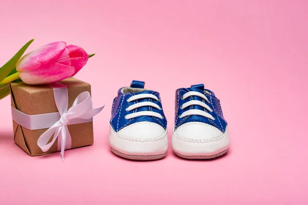 Botitas de bebé, caja de regalo y tulipán sobre fondo rosa, concepto de día de las madres - foto de stock