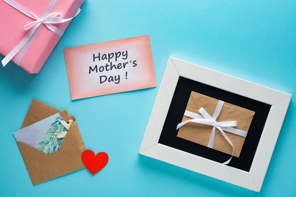 Top view of gift box, envelopes and greeting cards with happy mothers day lettering on blue background — Stock Photo