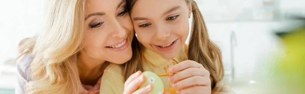 Tiro panorámico de niño lindo pintando huevo de Pascua cerca de madre feliz - foto de stock