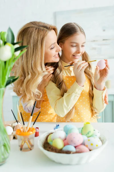 Enfoque selectivo de niño alegre pintura huevo de Pascua cerca de la madre - foto de stock