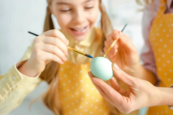 Selective focus of happy daughter and mother painting easter egg — Stock Photo