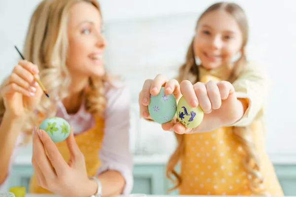 Selective focus of happy kid holding painted easter eggs near mother — Stock Photo