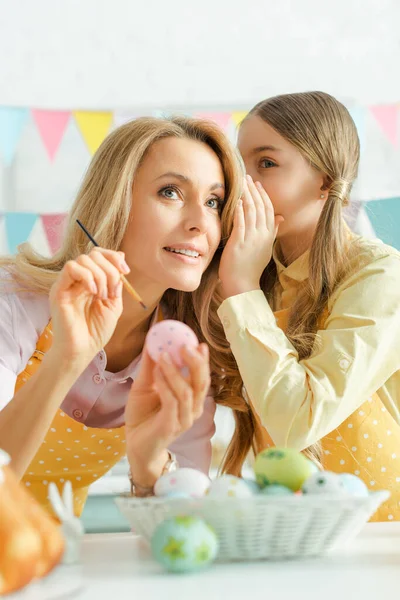 Selective focus of kid whispering in ear of mother near easter eggs — Stock Photo