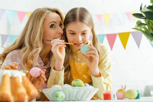 Selektiver Fokus der Mutter lächelnd neben fröhlicher Tochter beim Bemalen von Ostereiern — Stockfoto