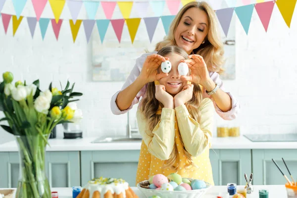 Glückliche Mutter bedeckt Augen ihrer Tochter mit bemalten Ostereiern — Stockfoto