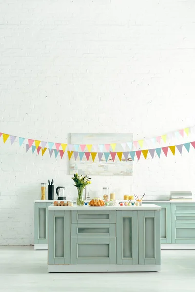 Modern kitchen with baked easter cake, painted chicken eggs and flowers in vase — Stock Photo