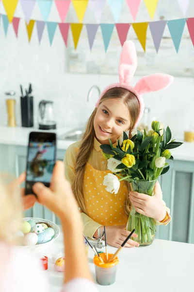 Foco selectivo de la madre tomando fotos de hija en orejas de conejo con tulipanes - foto de stock