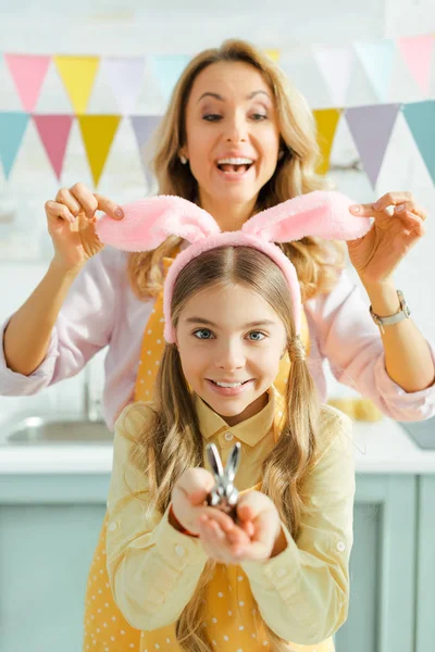 Foco selectivo de la madre alegre tocando orejas de conejo en la hija feliz sosteniendo conejo decorativo - foto de stock