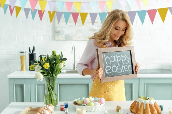 Mujer alegre sosteniendo pizarra con letras de Pascua feliz - foto de stock