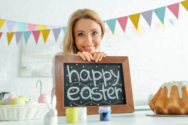 Enfoque selectivo de la mujer sonriente sosteniendo pizarra con letras de Pascua feliz - foto de stock