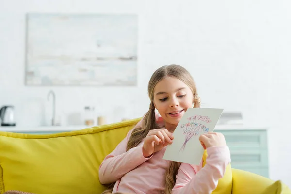 Niño alegre mirando la tarjeta de felicitación con letras felices del día de las madres - foto de stock