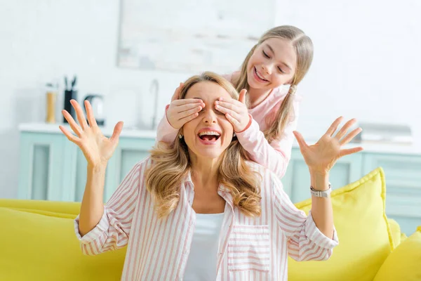 Happy kid covering eyes of surprised mother gesturing in living room — Stock Photo