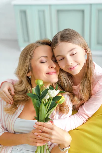 Linda hija abrazando feliz madre con ramo de tulipanes - foto de stock