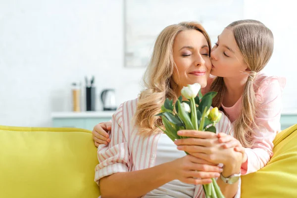 Cute daughter kissing happy mother holding bouquet of tulips — Stock Photo