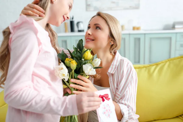 Messa a fuoco selettiva di madre felice guardando figlia con fiori e biglietto di auguri — Foto stock