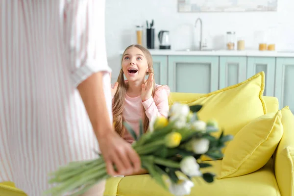 Selective focus of surprised kid looking at mother with flowers — Stock Photo