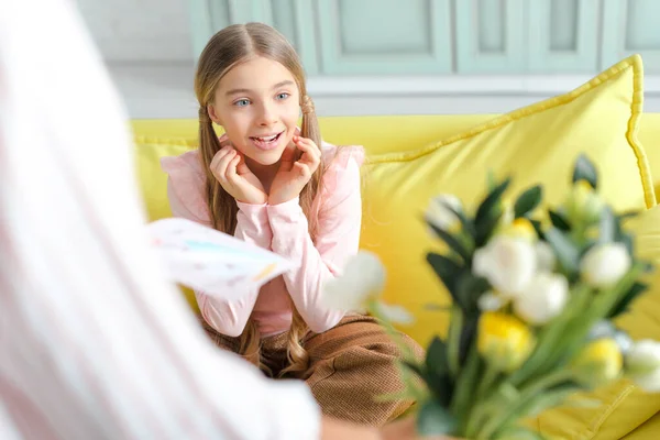 Selective focus of surprised kid looking at flowers in hand of mother — Stock Photo