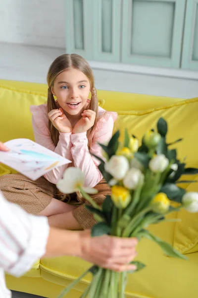 Selective focus of surprised child looking at flowers in hand of mother — Stock Photo