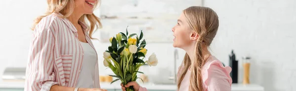 Tiro panorâmico de criança feliz dando flores à mãe alegre em casa — Fotografia de Stock