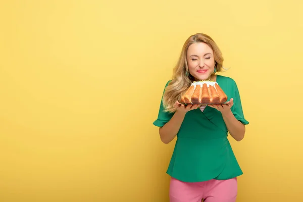 Mulher sorridente com olhos fechados segurando saboroso bolo de Páscoa isolado no amarelo — Fotografia de Stock
