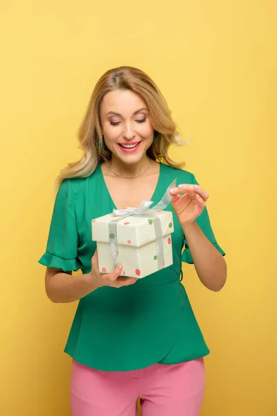 Mujer sonriente sosteniendo caja de regalo aislada en amarillo - foto de stock