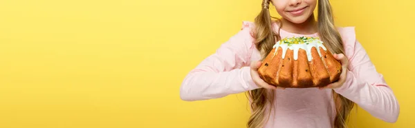 Panoramaaufnahme eines glücklichen Kindes, das Osterkuchen isoliert auf gelb hält — Stockfoto