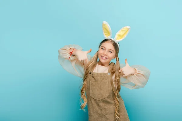 Bambino allegro con orecchie di coniglio mostrando pollici in alto isolato su blu — Foto stock