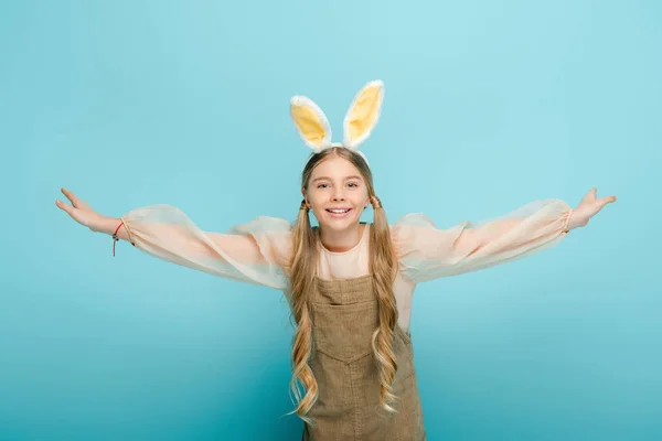 Enfant positif avec des oreilles de lapin et les mains tendues isolé sur bleu — Photo de stock
